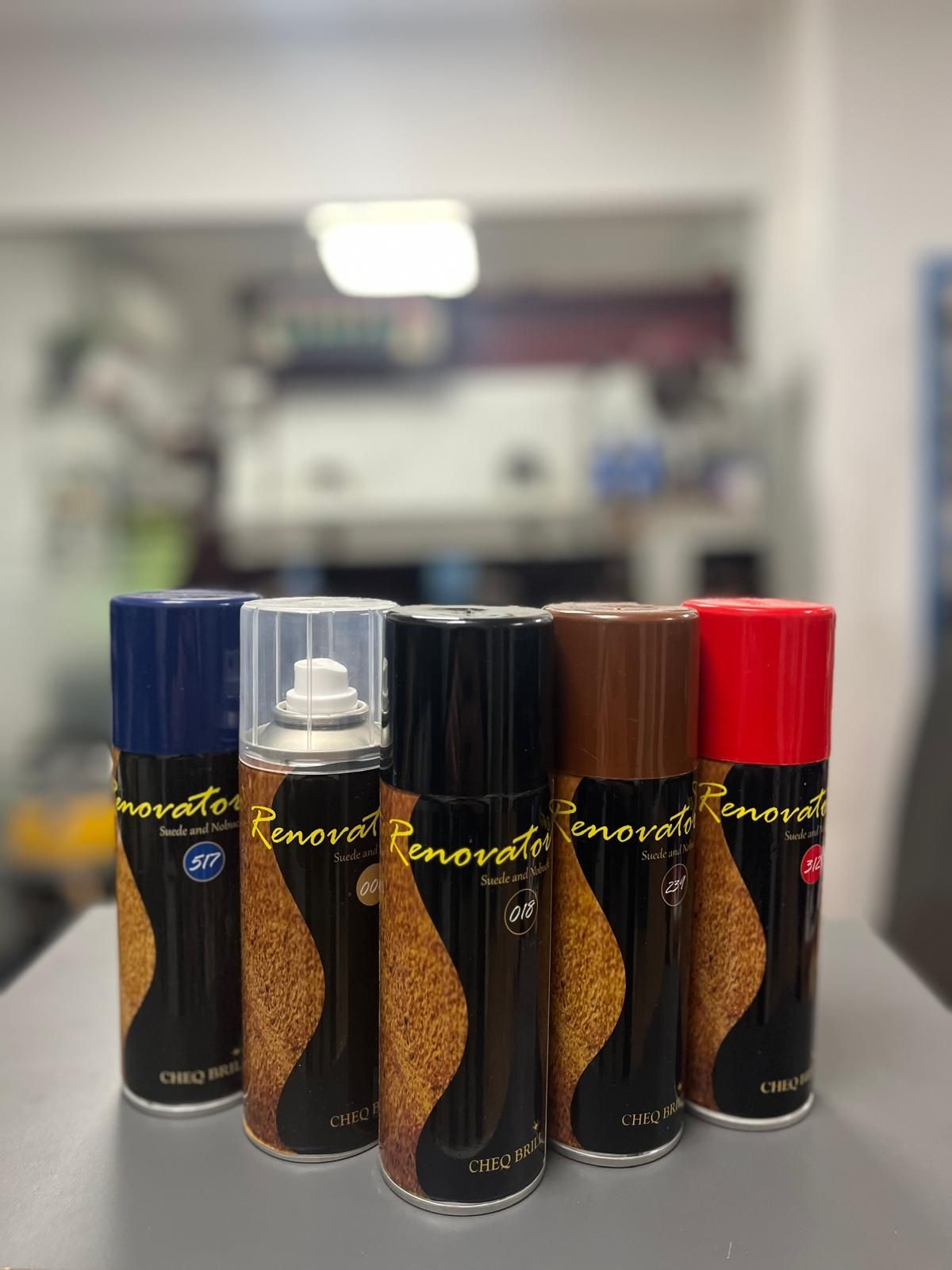 Five cans of Renovator spray in various colors on a table in a blurred background room.