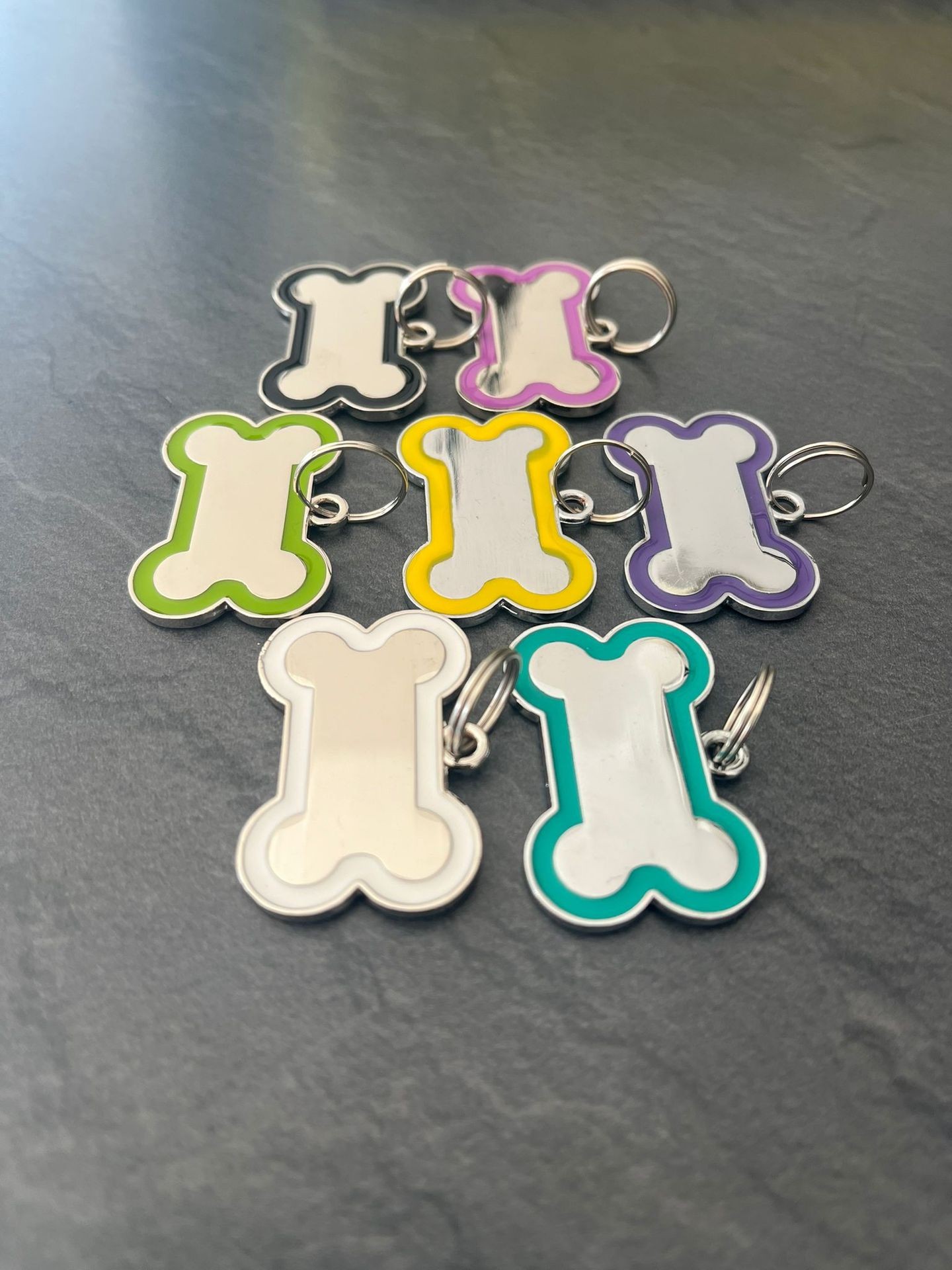 Colorful bone-shaped metal keychains on a gray surface.