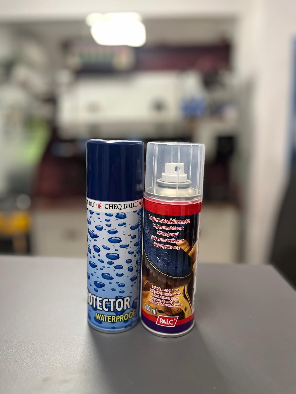 Two cans of waterproof spray protectors on a counter in a blurred indoor setting.