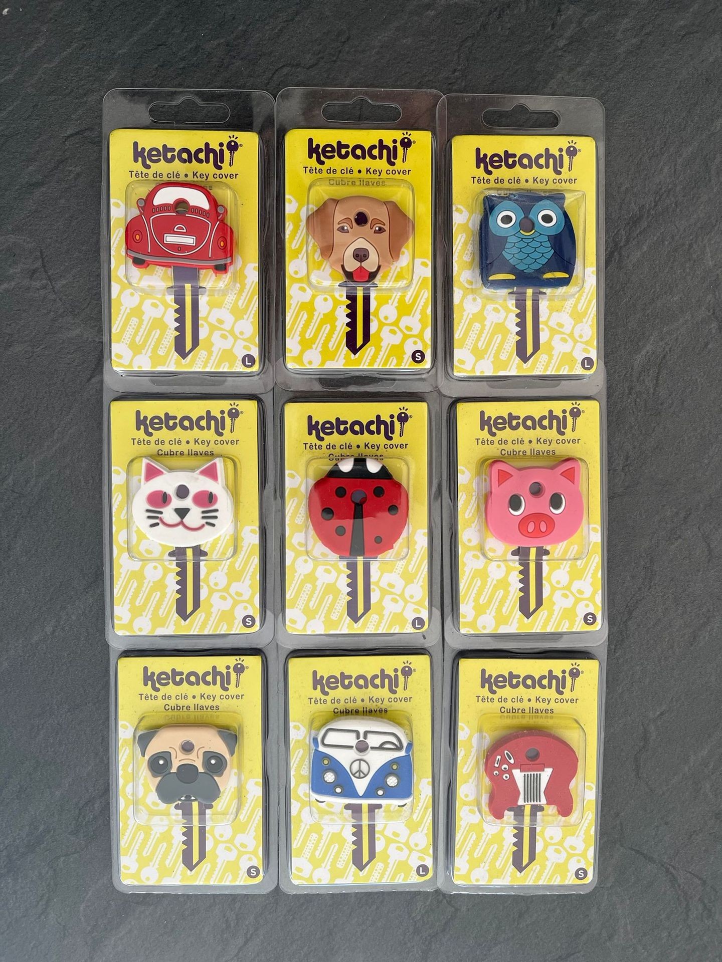 Nine key covers in packaging featuring various designs like animal faces and vehicles against a yellow background.